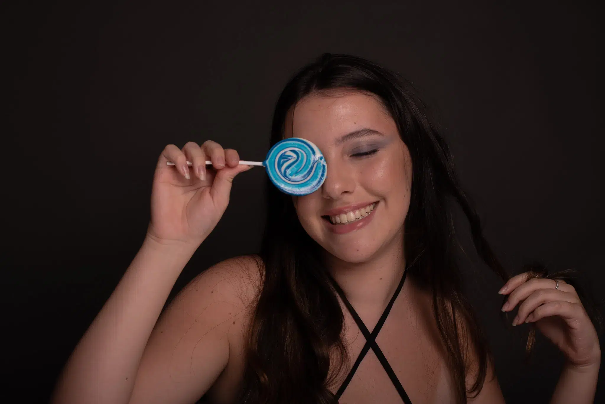 Transforme suas fotos com uma pós-produção humanizada e profissional 7 Modelo sorrindo e segurando pirulito azul, antes da pós-produção